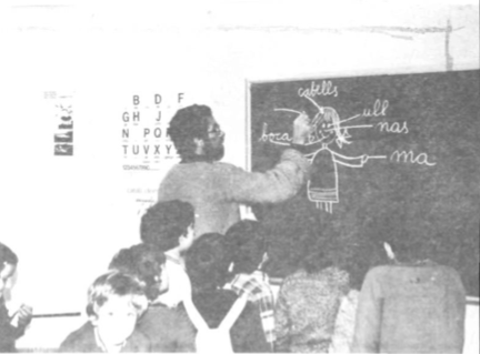 Imatge d'una aula amb alumnes i una pissarra amb lletres i dibuixos