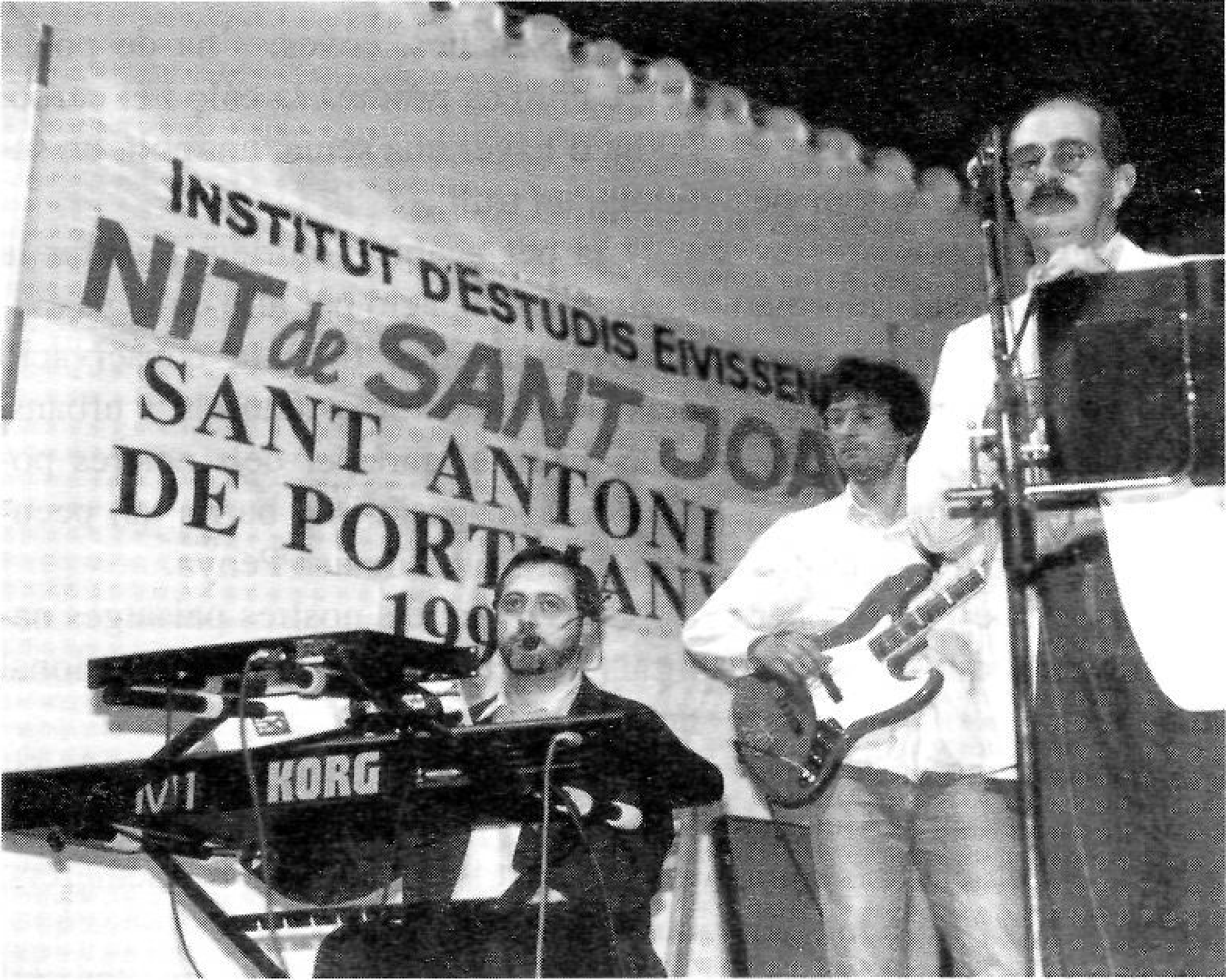 Jaume Arnella cantant amb un micròfon a l'escenari. Rètol parcial al fons: D'ESTUDIS ...ANT ANTONI ...TMANY.