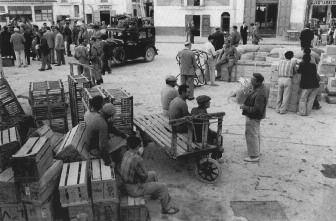 El port d'Eivissa era l'epicentre de l'economia comercial que s'havia desenvolupat durant el primer terç del segle xx i que revifà en els anys 50, en acabar-se els anys de la fam». Els treballadors que esperen el vaixell seuen a sobre de les caixes utilitzades per exportar ous; més enllà veiem caixes per a gallines i, al fons, un taxi