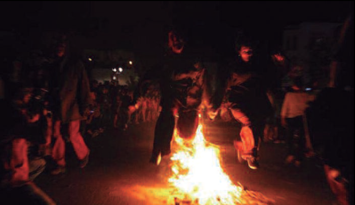 Gran foguera nocturna amb flames altes, envoltada de siluetes de persones.