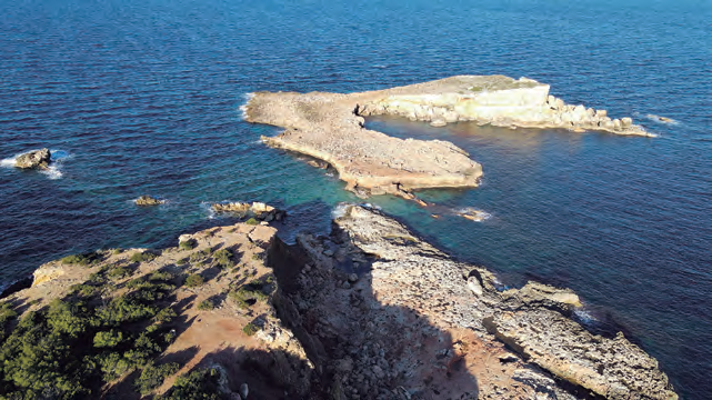 Fotografia aèria de la punta de l'illa d'Encalders, en primer terme, amb la plana de s'llla a la part dreta i, separada per l'estret pas de s'llla, al centre de la imatge, l'illa d'Encalders (fotografia d'Iñaki de Eróstegui Aznar).