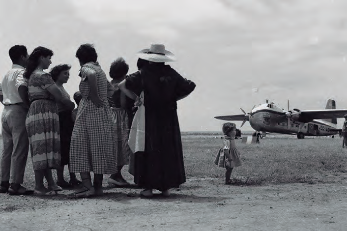 Un grup de persones observant un avió d'hèlix en una pista d'aterratge.